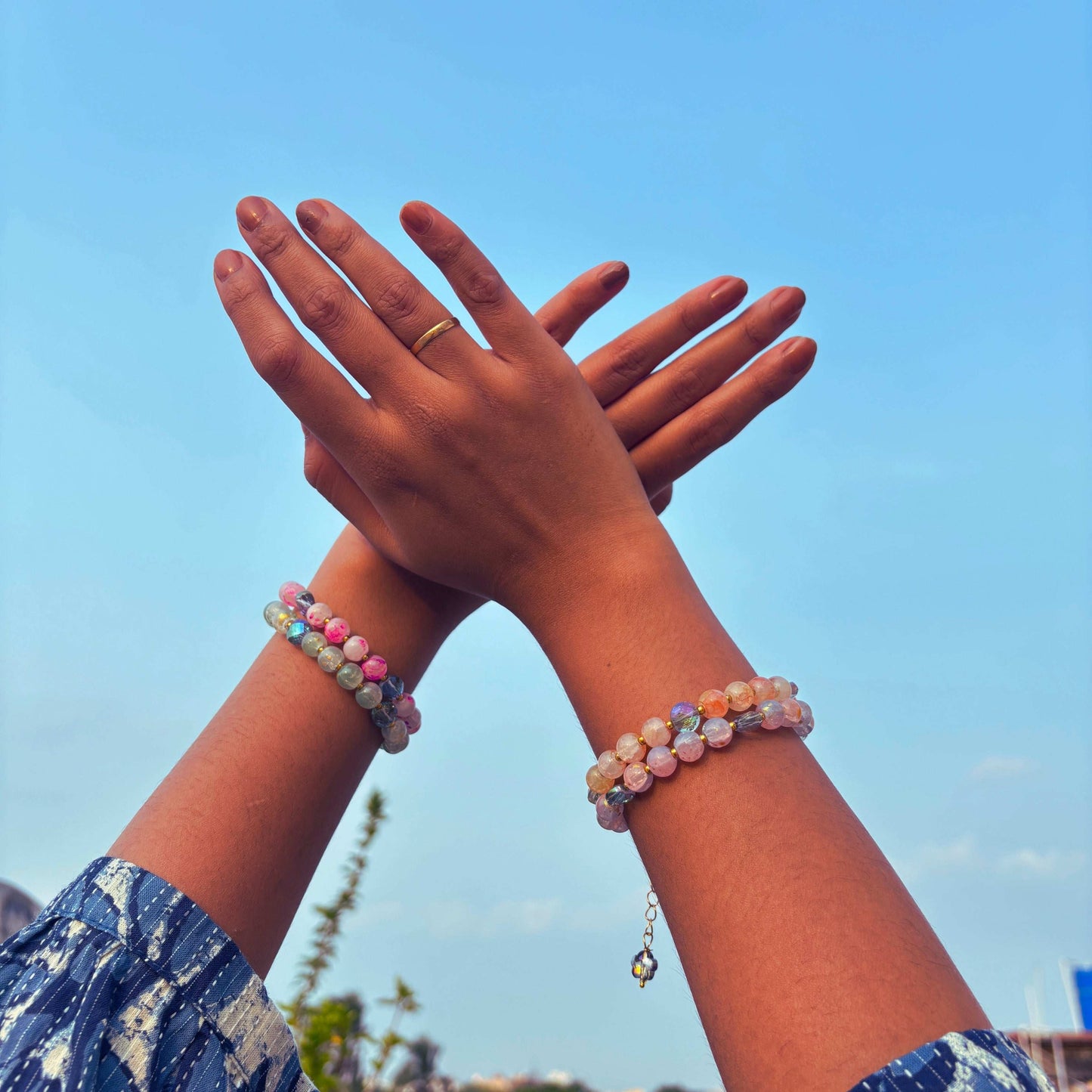 Two hands wearing a Marble Effect Beaded Bracelet Combo against a blue sky backdrop