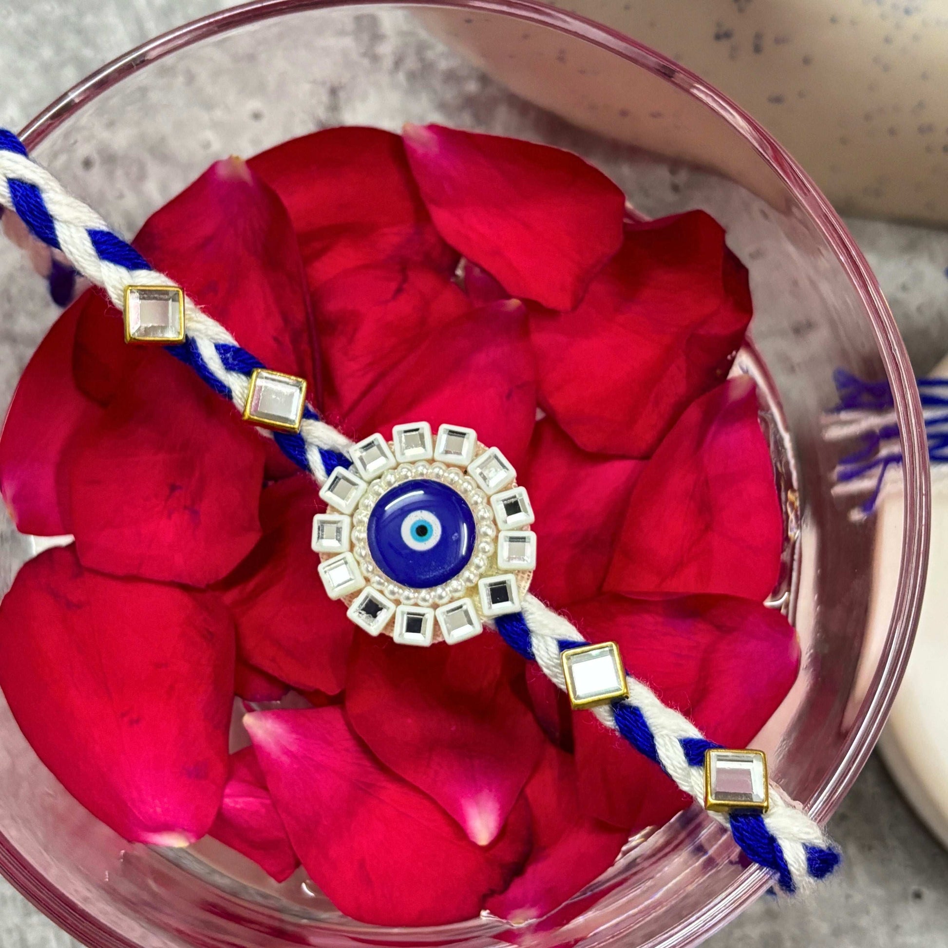 Evil Eye Designer Rakhi Raksha Bandhan 2025 with decorative elements on a bed of rose petals